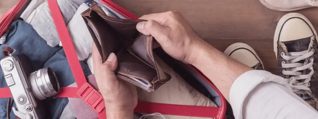 Man looking in an empty wallet while packing his bag for vacation.