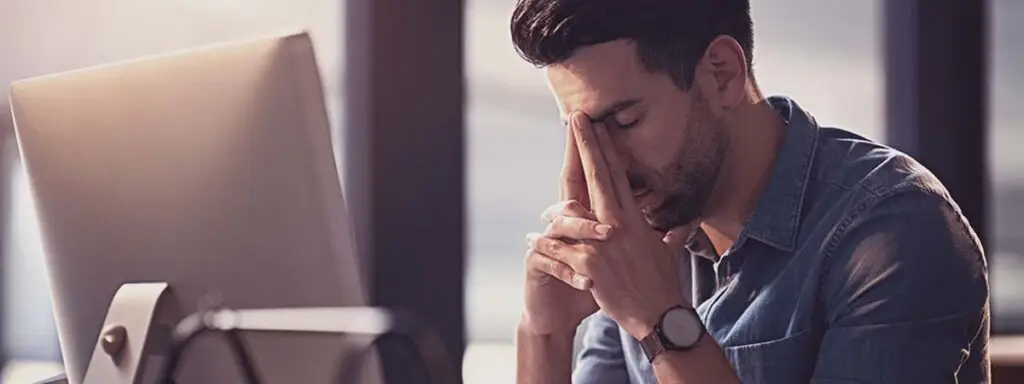 Man in front of computer distressed with hands resting on face