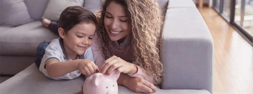 Mother and young son on the couch putting coins in a piggy bank.