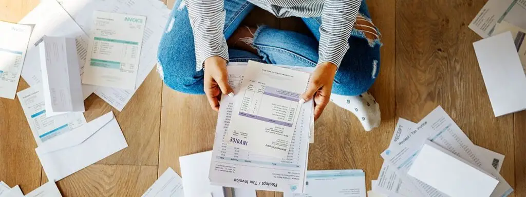 Person sitting on the floor overwhelmed by debt paperwork